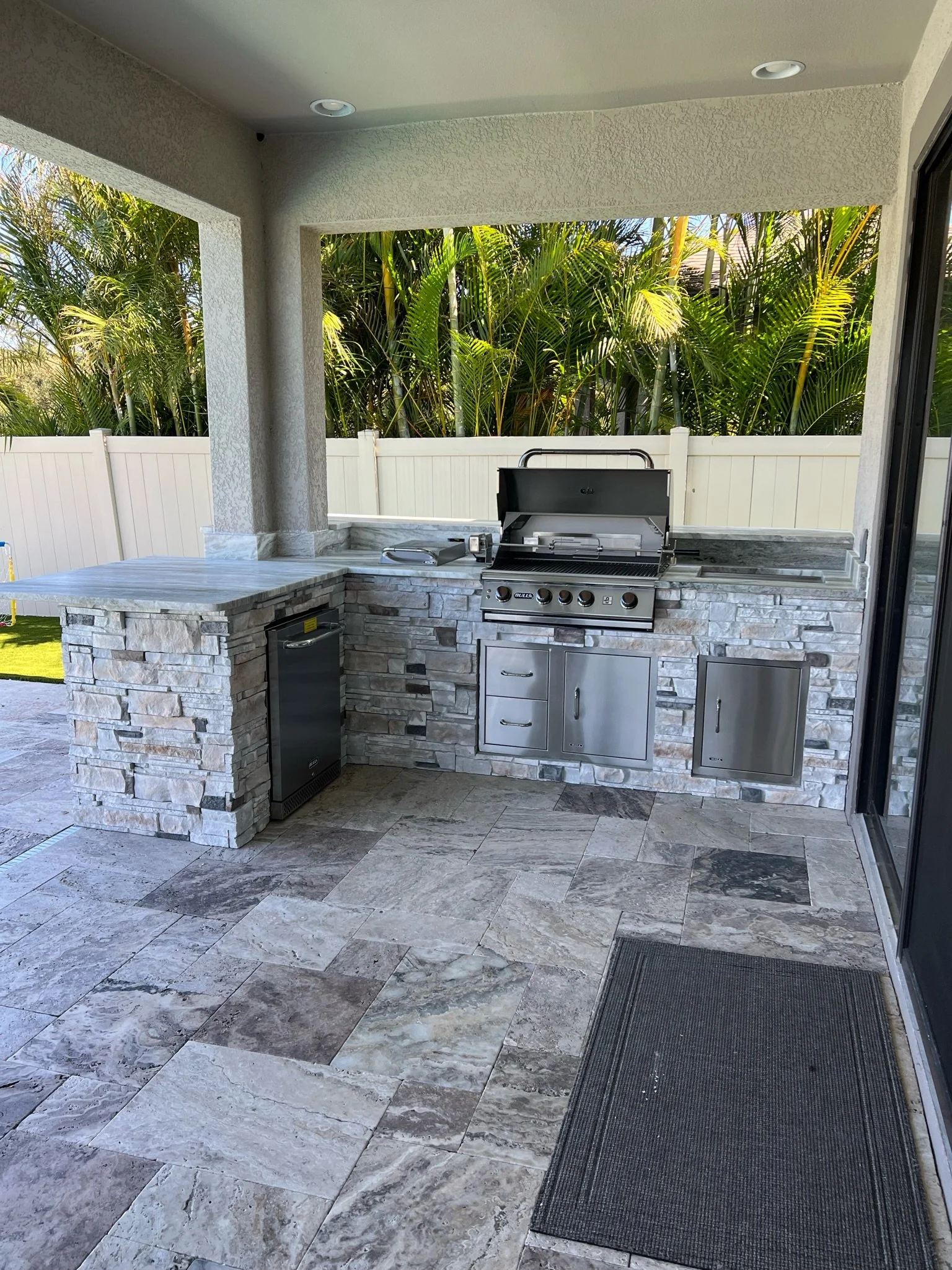 Finished outdoor kitchen with stone counter, grill and small fridge